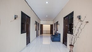 A hallway with a blue sofa, a vase with branches, and a door at the end. - Hotel O Graha 99 (Surabaya)