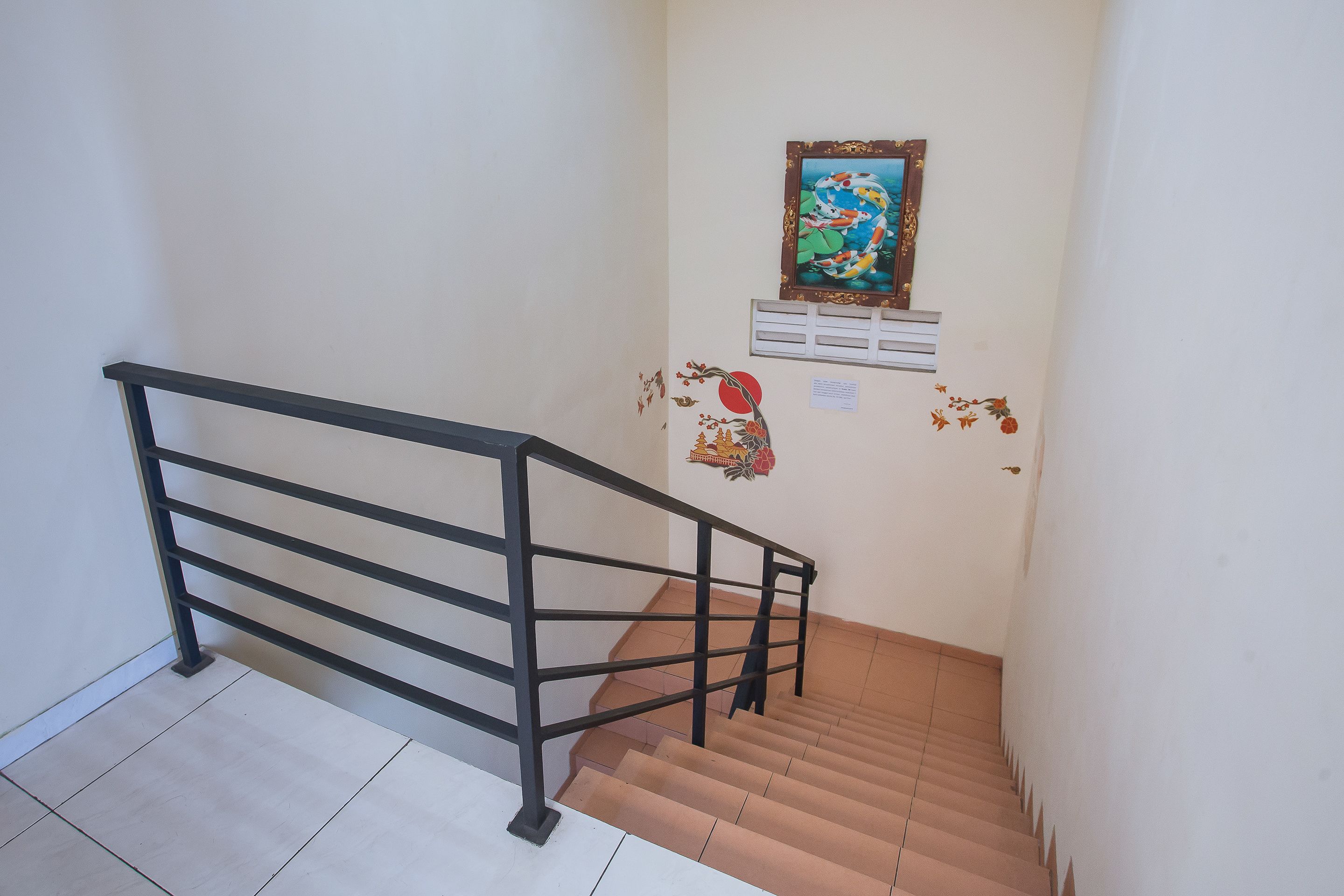 A staircase with a black metal railing, a tiled floor, and a wall with a framed picture and some wall stickers.