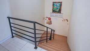 A staircase with a black metal railing, a tiled floor, and a wall with a framed picture and some wall stickers. - Hotel O Graha 99 (Surabaya)