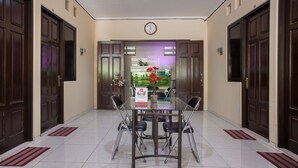 A hotel dining area with a glass table, four chairs, a clock on the wall, and a view of a garden through the glass door. - Hotel O Graha 99 (Surabaya)