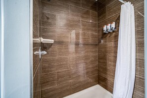 Ein Duschbereich mit Badewanne, weißem Vorhang und Ablage für Toilettenartikel.