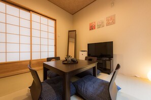 A traditional Japanese room with tatami flooring, a low table with cushions, a television, and a sliding door.