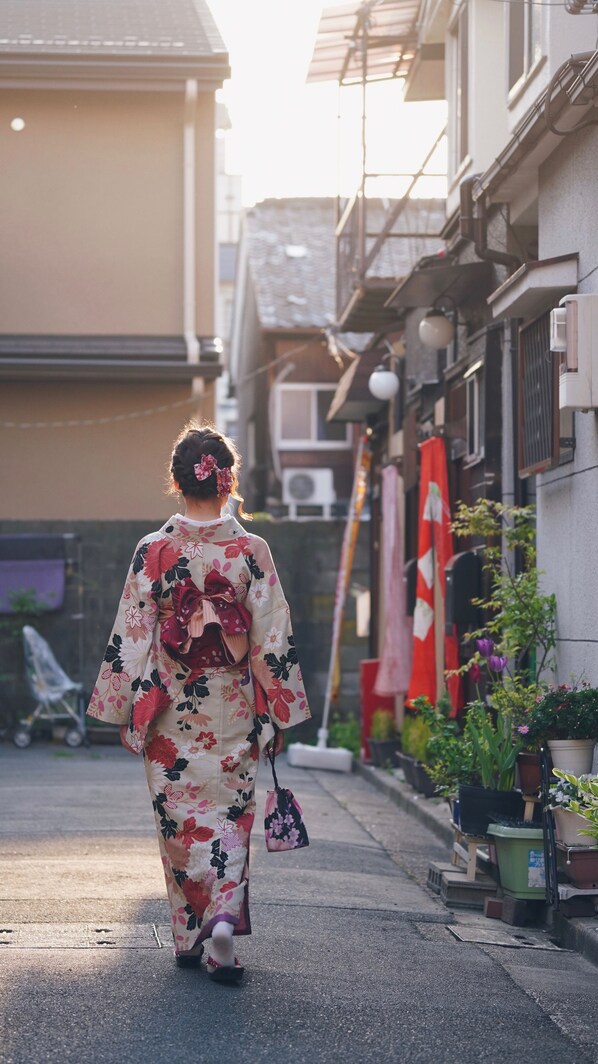 A person in traditional attire walking down a street lined with buildings and potted plants.