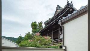 Un bâtiment de style japonais traditionnel, doté d’une terrasse en bois, d’une chaise blanche et offrant une vue sur la verdure et une pagode en arrière-plan.