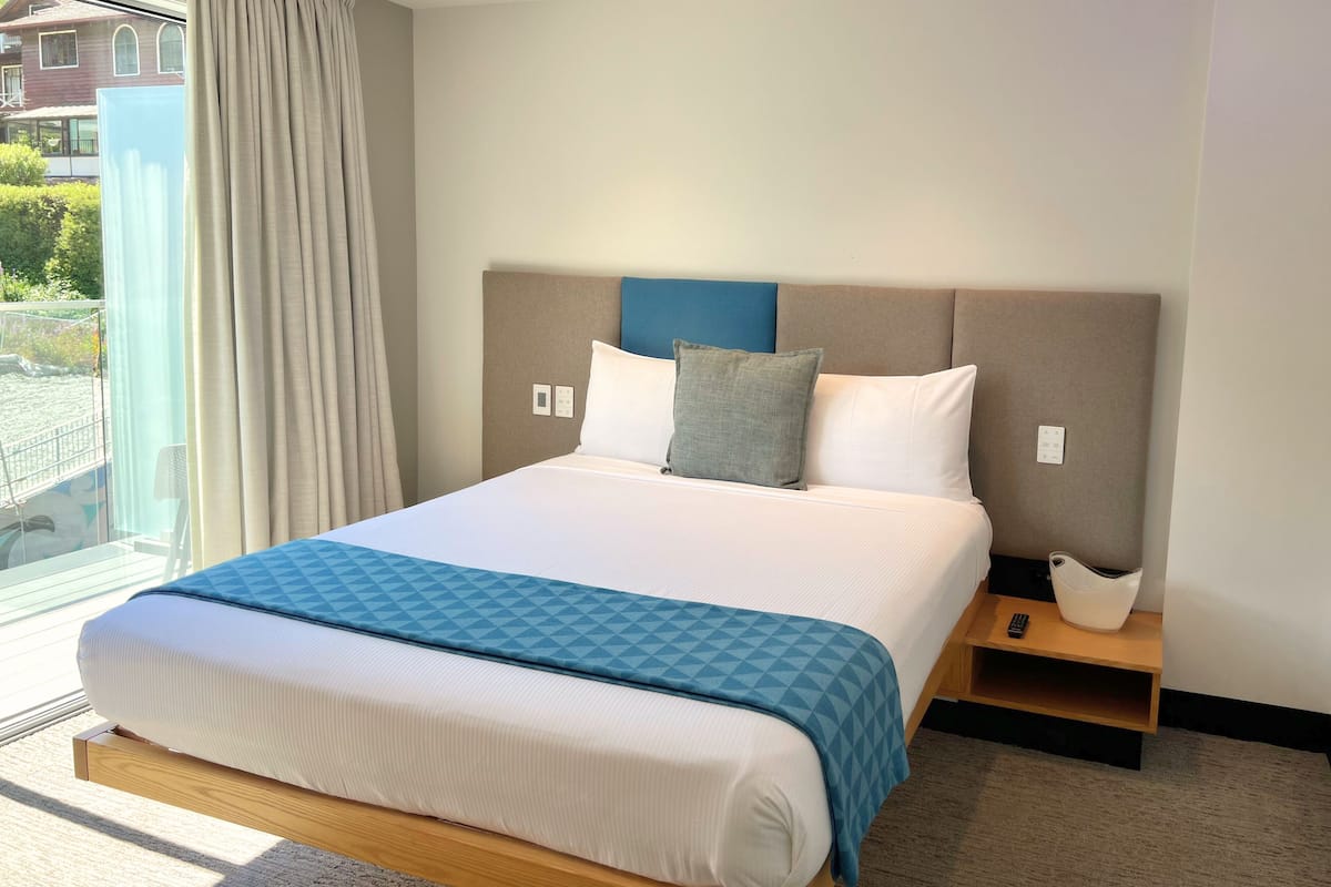 Quarto de hotel moderno com uma cama grande, uma mesa de cabeceira e vista para o exterior.