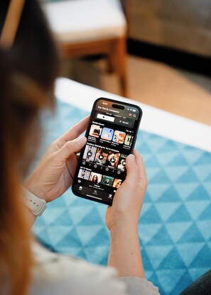 A person holding a smartphone displaying a TV show interface. - Mi-pad Queenstown (Queenstown)