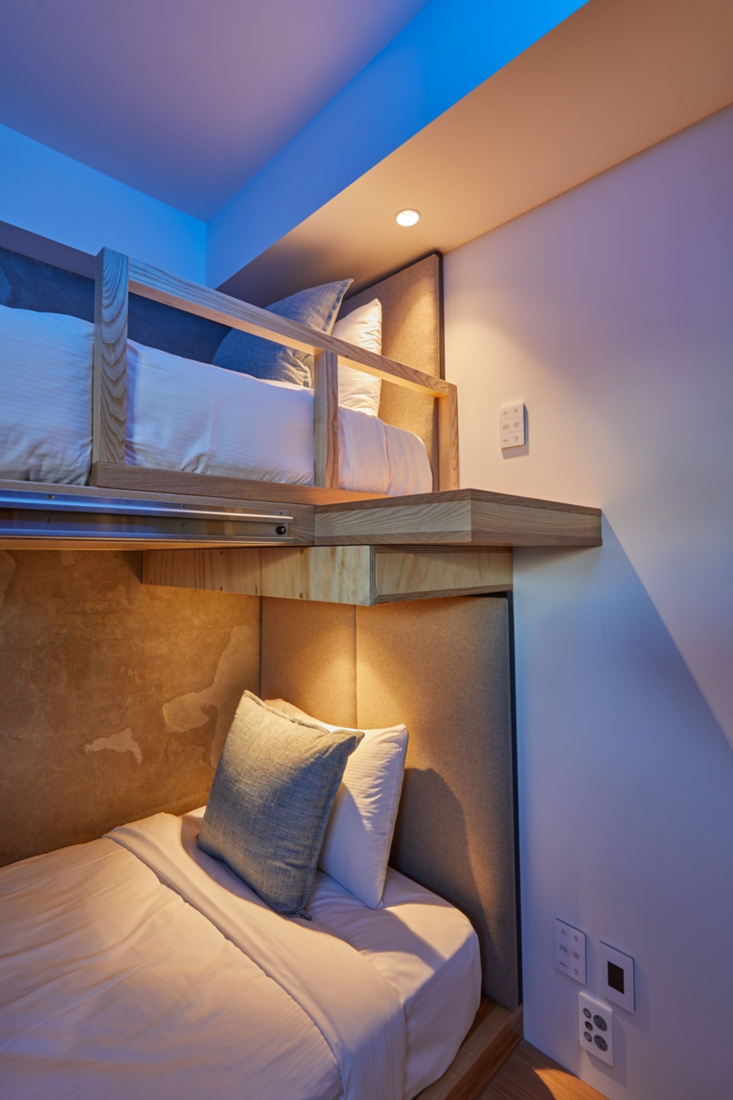 A bunk bed with a lower bed below, a headboard, and a wall-mounted light fixture.