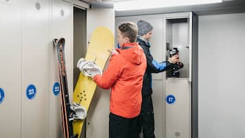 A locker room with numbered lockers, a yellow snowboard, and a person holding skis.