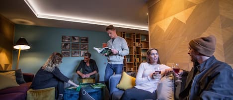 A group of people in a modern lounge area with sofas, a coffee table, and a bookshelf.