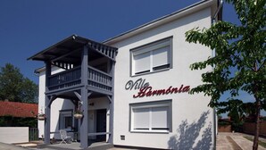 A two-story building with a balcony, a sign reading "Villa Harmonia," and a small outdoor seating area.