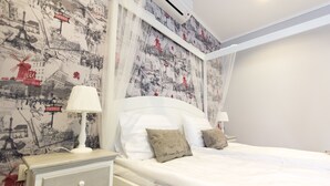 A bedroom with a bed, two bedside tables, a nightstand, and a wall with a cityscape wallpaper.