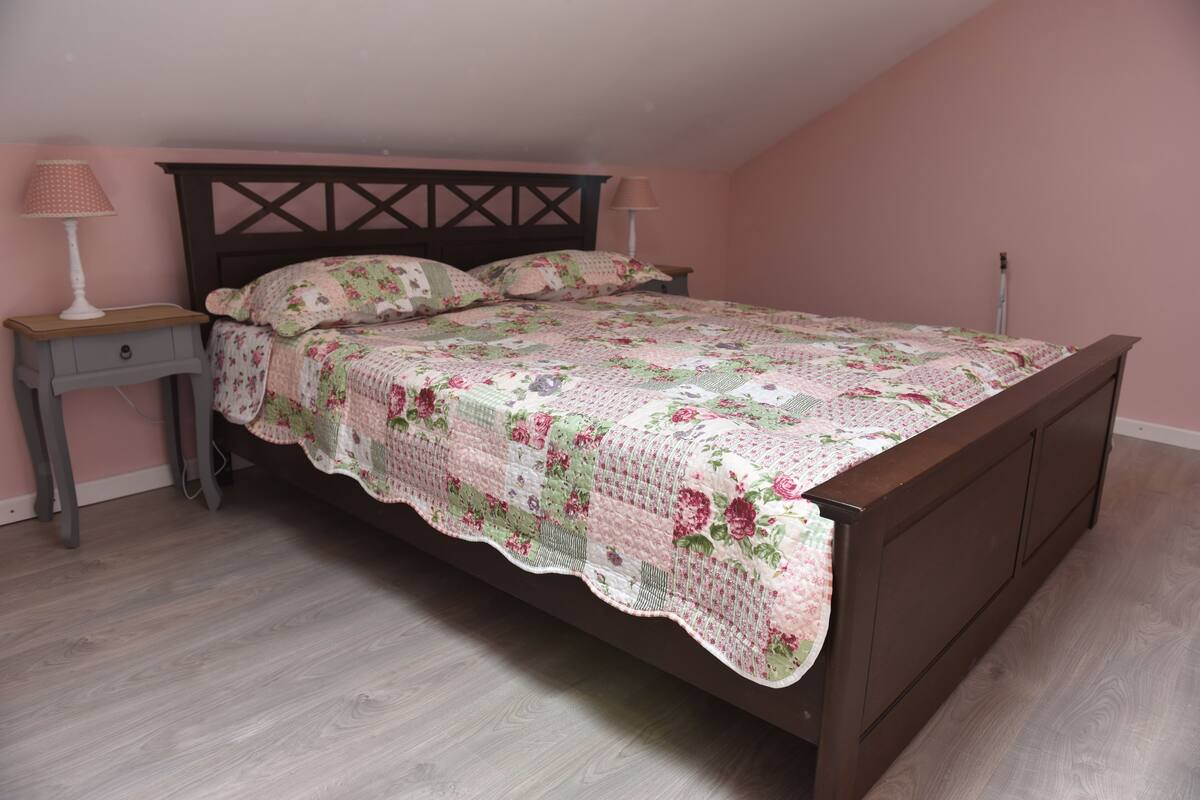 A bedroom with a wooden bed, floral bedding, a nightstand, and a lamp.