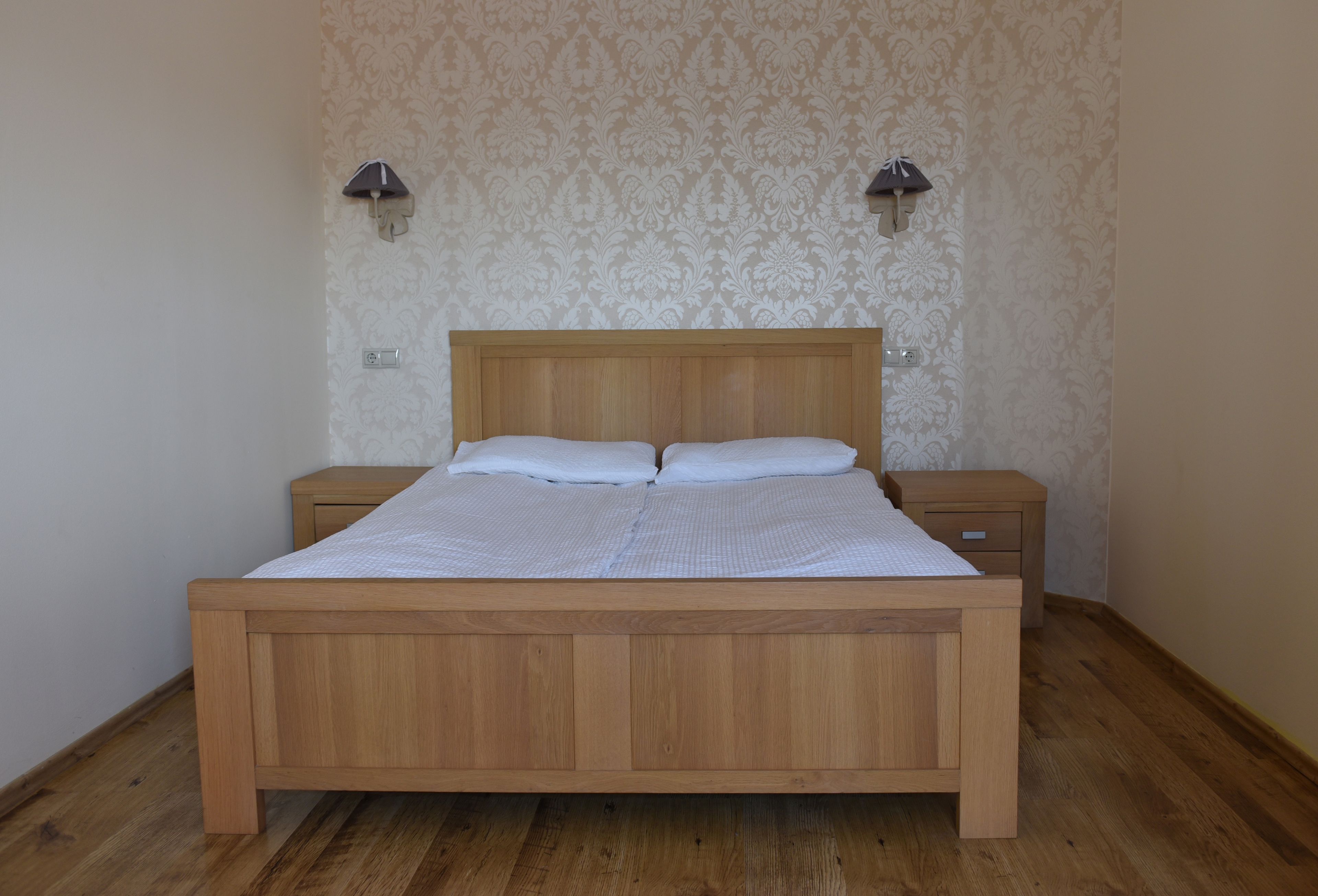 A wooden bed with a headboard, two bedside tables, and a patterned wallpaper.