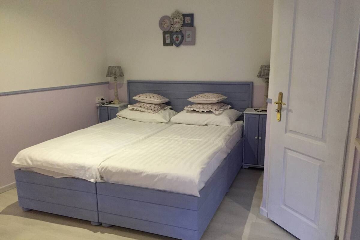 A bedroom with a single bed, two bedside tables, a nightstand, and a door.