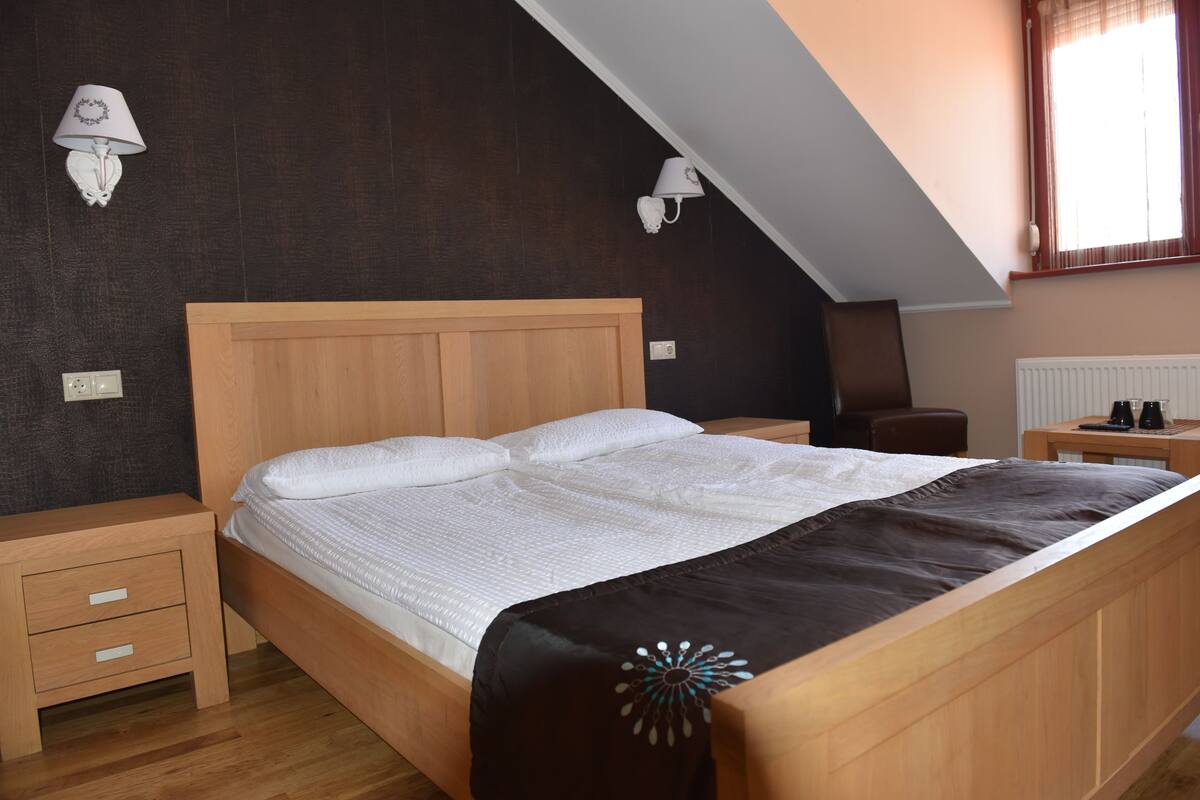 A bedroom with a wooden bed, nightstands, a desk, and a window with curtains.