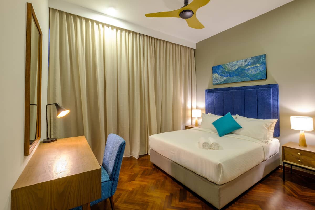 A hotel room with a bed, a desk, a chair, a ceiling fan, and a painting on the wall.