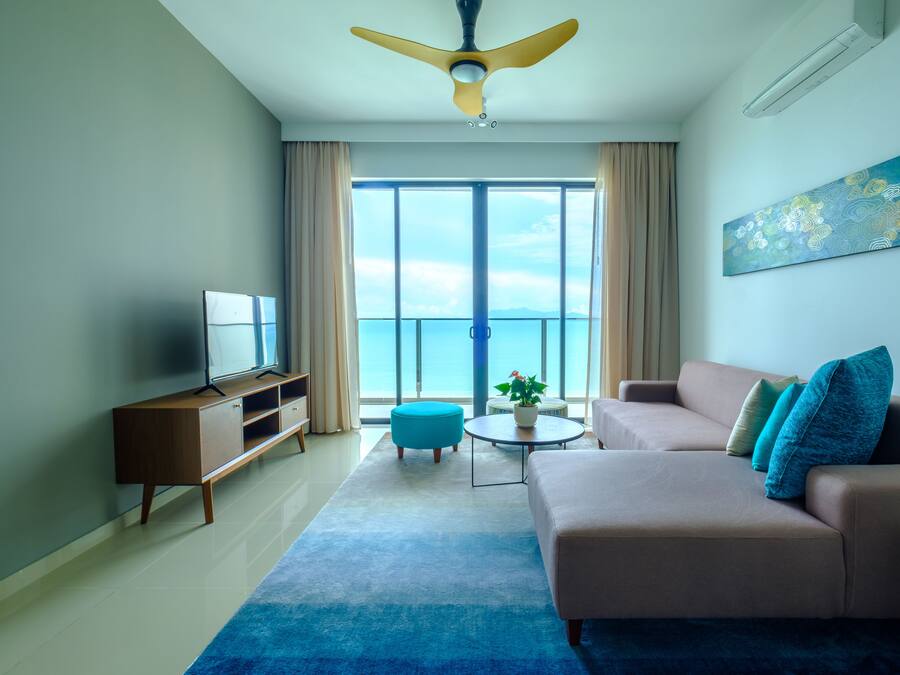 Una sala de estar moderna con un sofá, televisor, ventilador de techo y un ventanal con vistas al mar.