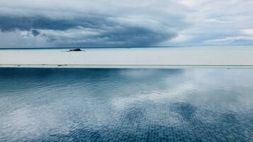 A clear view of a swimming pool with a tiled floor, a distant shoreline, and overcast skies.