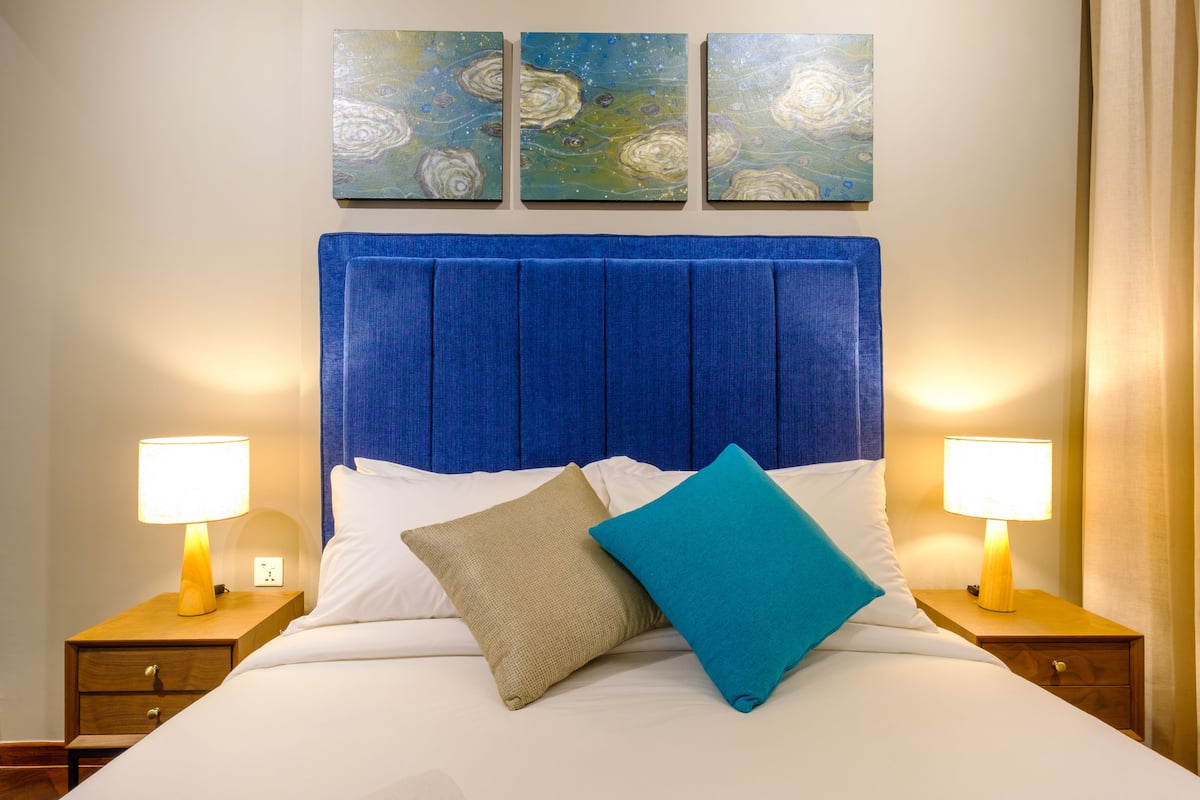 A bed with a blue headboard, white bedding, and two nightstands with lamps.