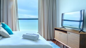 A hotel room with a bed, a TV on a wooden cabinet, and a view of the sea through large windows. - Tanjung Point Residences (George Town)
