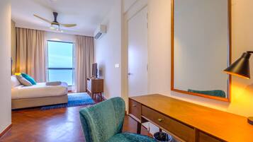 Une chambre d’hôtel comprenant un lit, un bureau, une chaise, un ventilateur de plafond, un grand miroir et une fenêtre avec des rideaux.