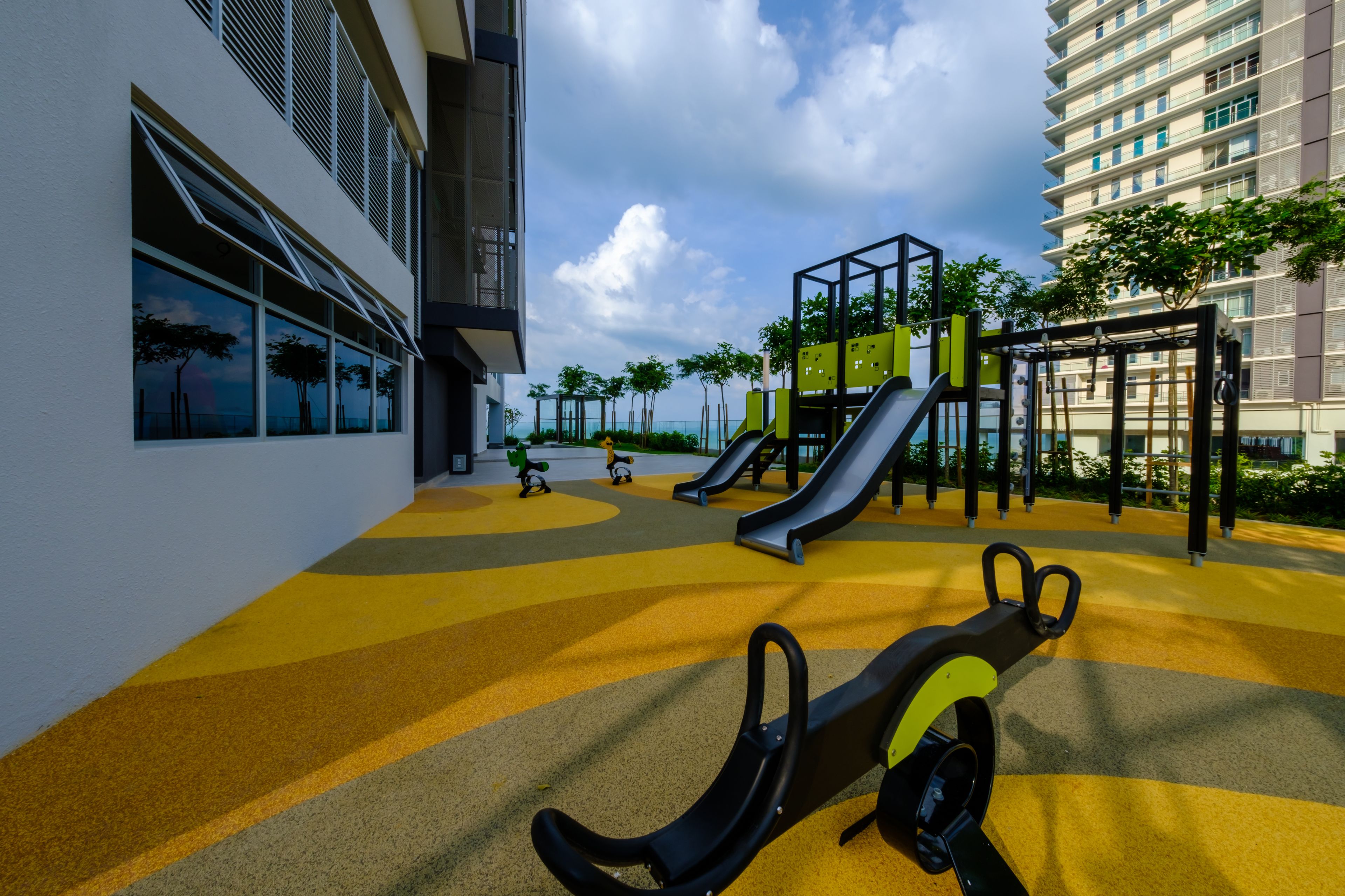 An outdoor playground with slides and exercise equipment, adjacent to a building with large windows and a yellow-tiled ground.