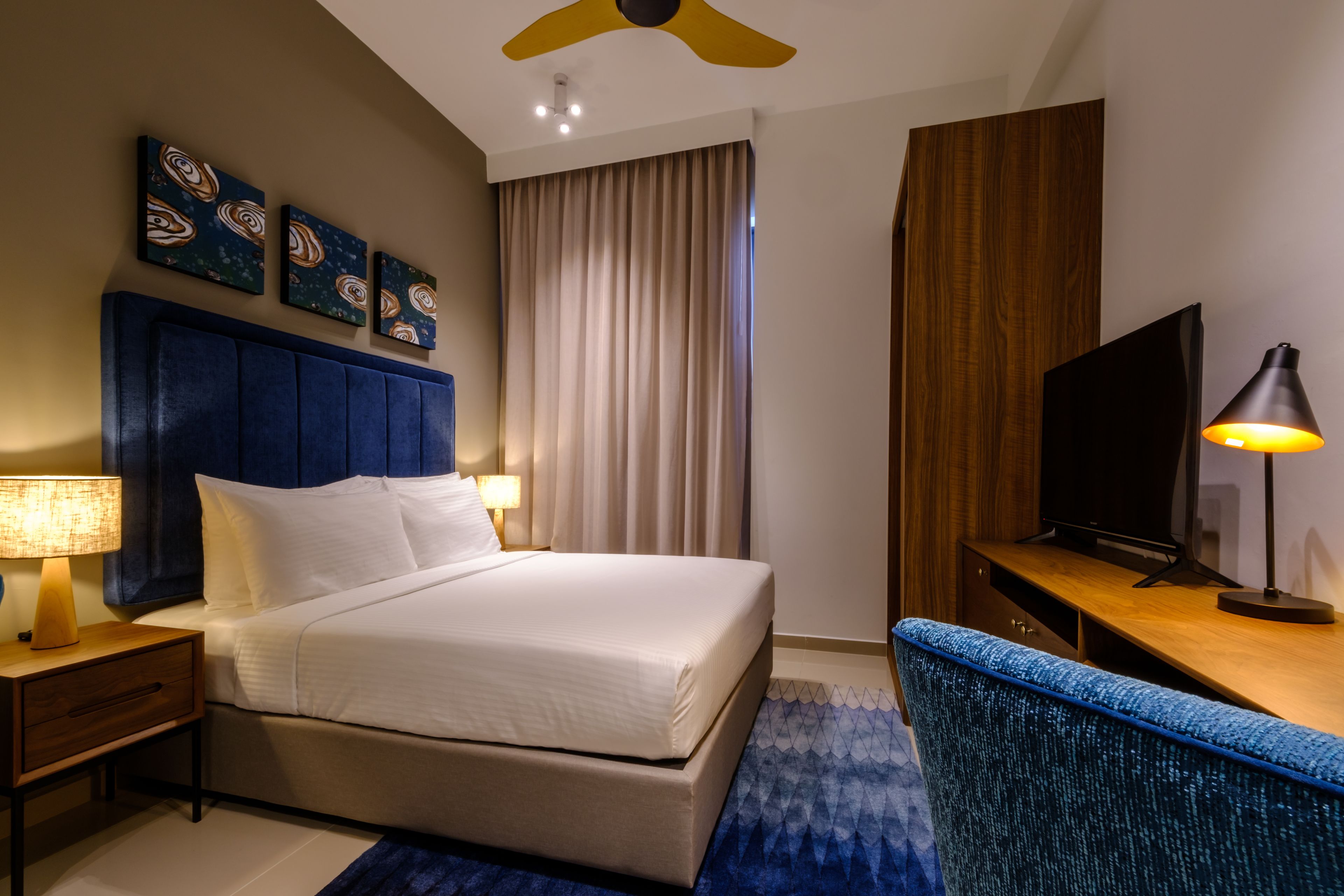 A hotel room with a bed, a desk, a television, and artwork on the wall.