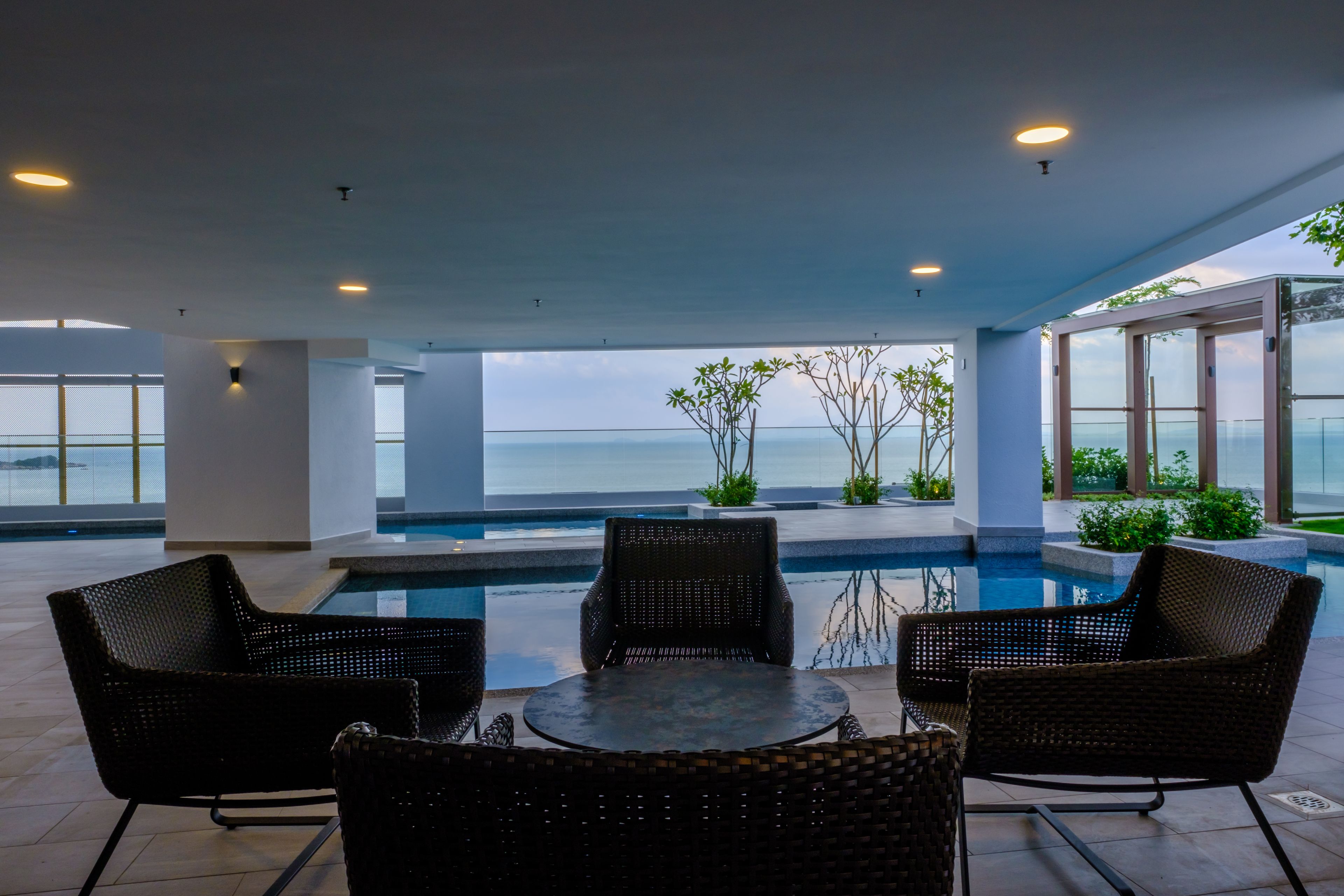 A modern outdoor pool area with wicker furniture and a view of the sea.