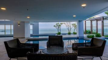 A modern outdoor pool area with wicker furniture and a view of the sea.