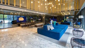 A spacious lobby with a blue seating area, a marble floor, and a high ceiling with hanging lights.