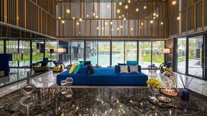A modern living room with a blue sofa, a glass coffee table, and a large window offering a view of a pool and greenery.