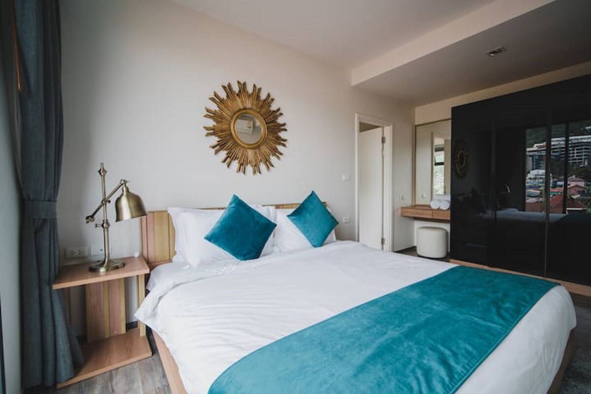Een moderne hotelkamer met een groot bed, een spiegel in de vorm van een zon, een bedlampje en uitzicht op het omliggende landschap.