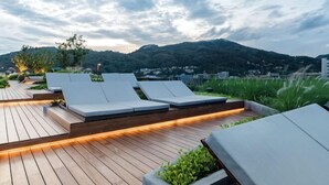 A rooftop terrace with sun loungers, wooden decking, and a view of a mountain.