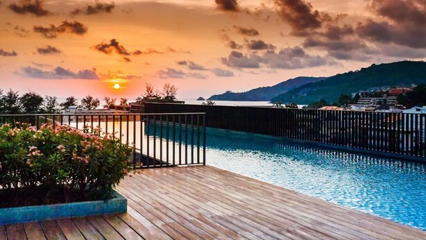 A swimming pool with a wooden deck and a view of the sunset over a hilly landscape.
