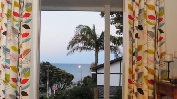 Una stanza con vista sul mare, palme e un edificio dalla facciata bianca.
