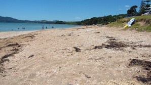 Una spiaggia con un litorale sabbioso, alcune persone e una tavola da surf appoggiata a una collinetta.