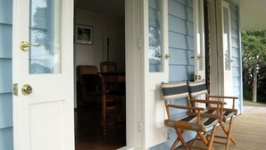 Un portico con due sedie di legno e una panca, una porta che dà su un ambiente interno e una finestra con vista sugli alberi.
