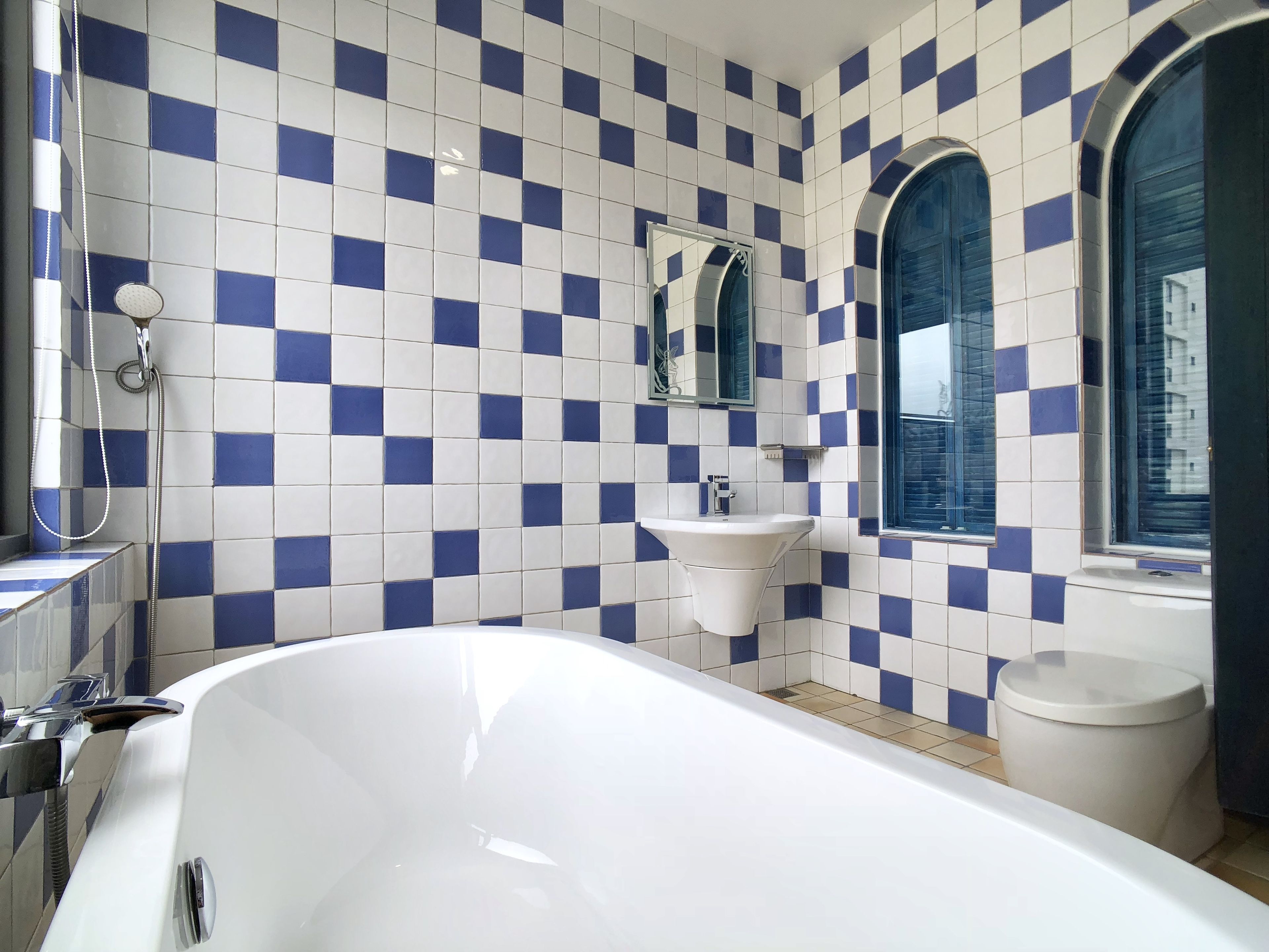 A bathroom with a white bathtub, a sink, and a toilet. The walls are tiled with a blue and white checkered pattern.