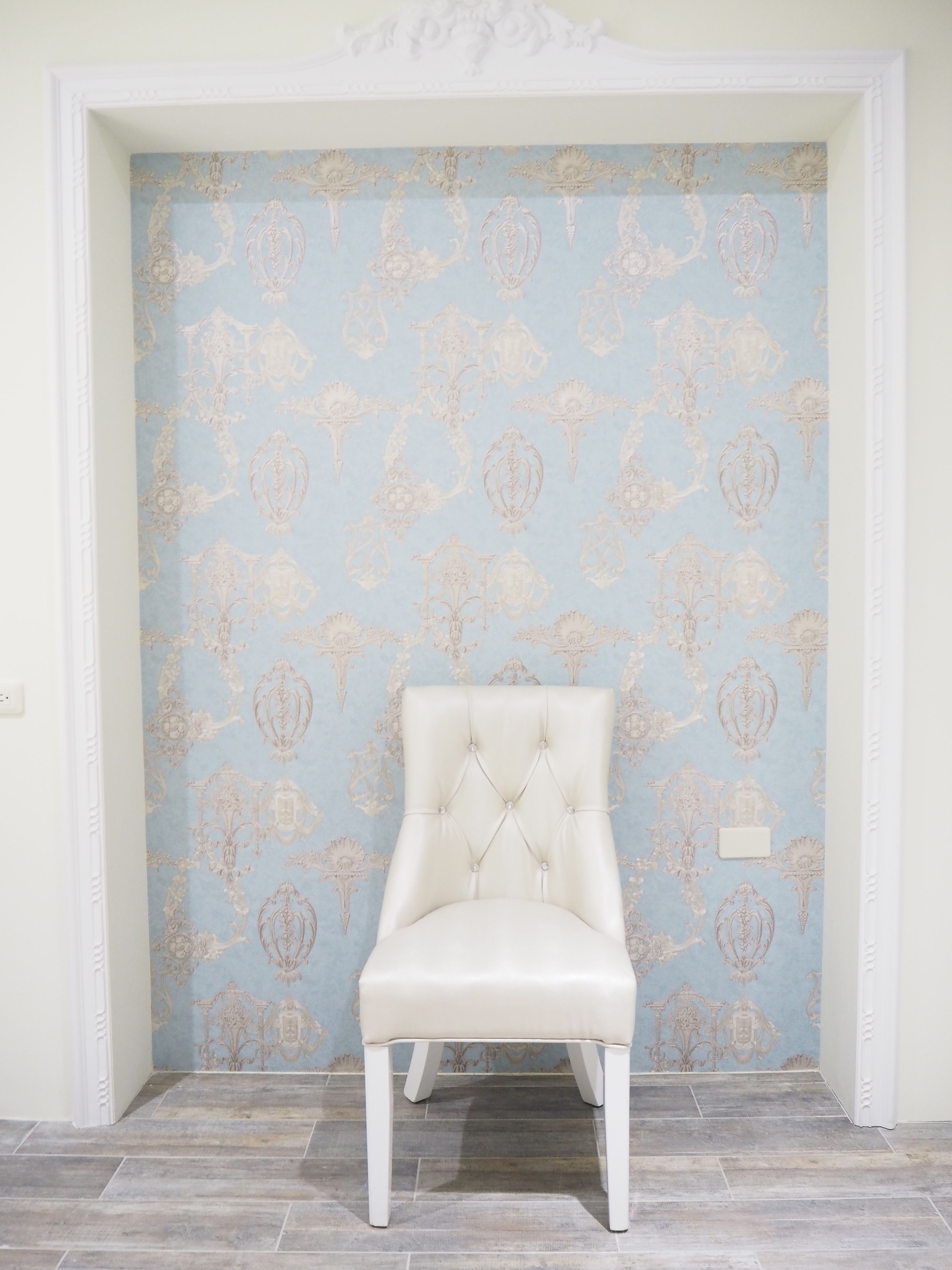 A chair in a corner with a patterned wallpaper and a white trim.