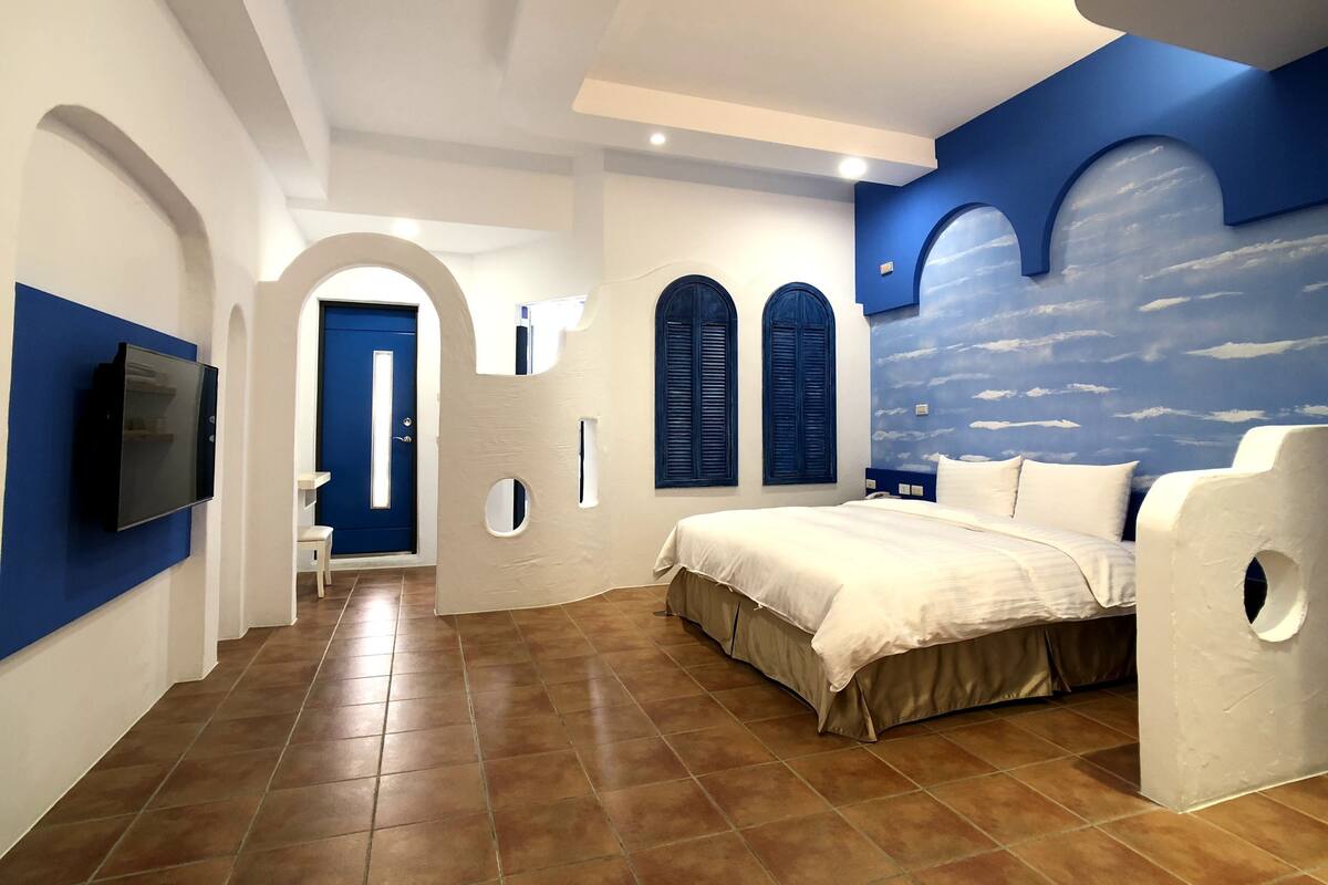 Une chambre à coucher avec un lit, un téléviseur et une fresque représentant des nuages sur le mur.
