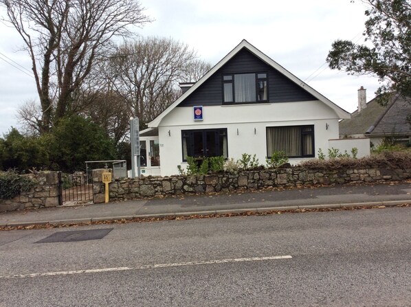 A two-story house with a white exterior and dark roof, featuring a stone wall in front and a metal gate. - Chy an Gwedhen (St Ives)