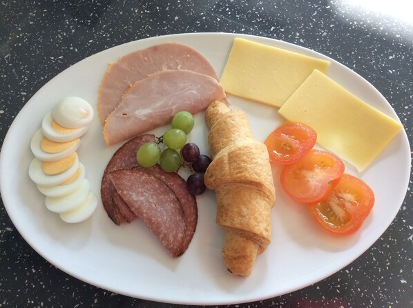 A plate with sliced ham, cheese, eggs, grapes, tomatoes, and a croissant. - Chy an Gwedhen (St Ives)