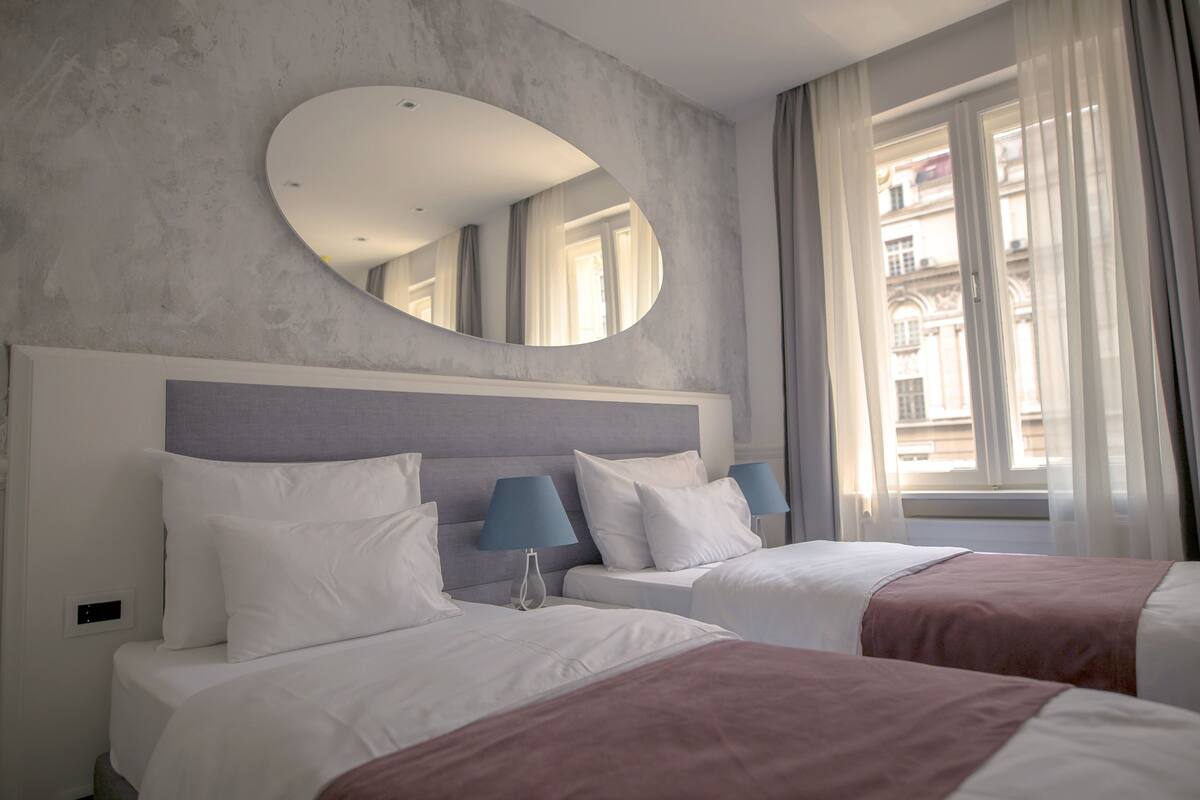 Habitación de hotel con dos camas, un espejo grande y una ventana con cortinas.
