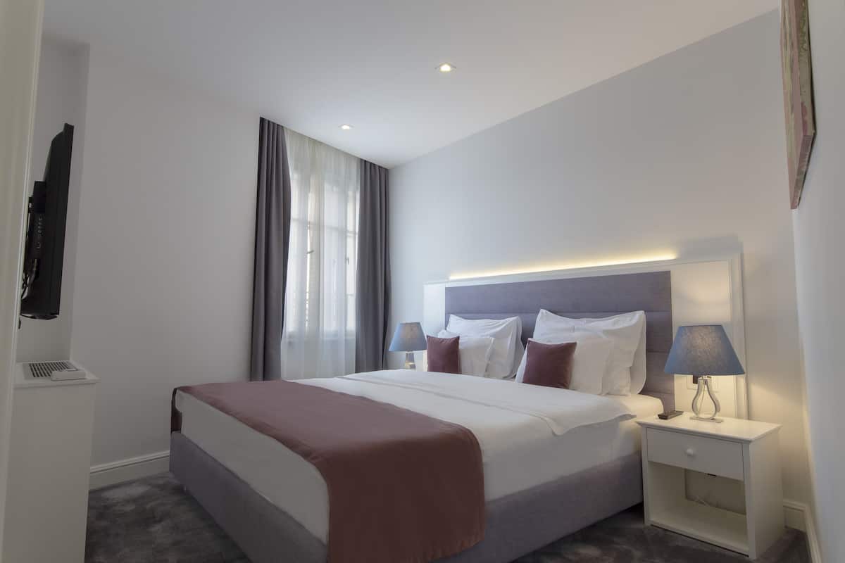 Una habitación de hotel moderna con una cama bien hecha, una mesita de noche con lámpara y una ventana con cortinas.