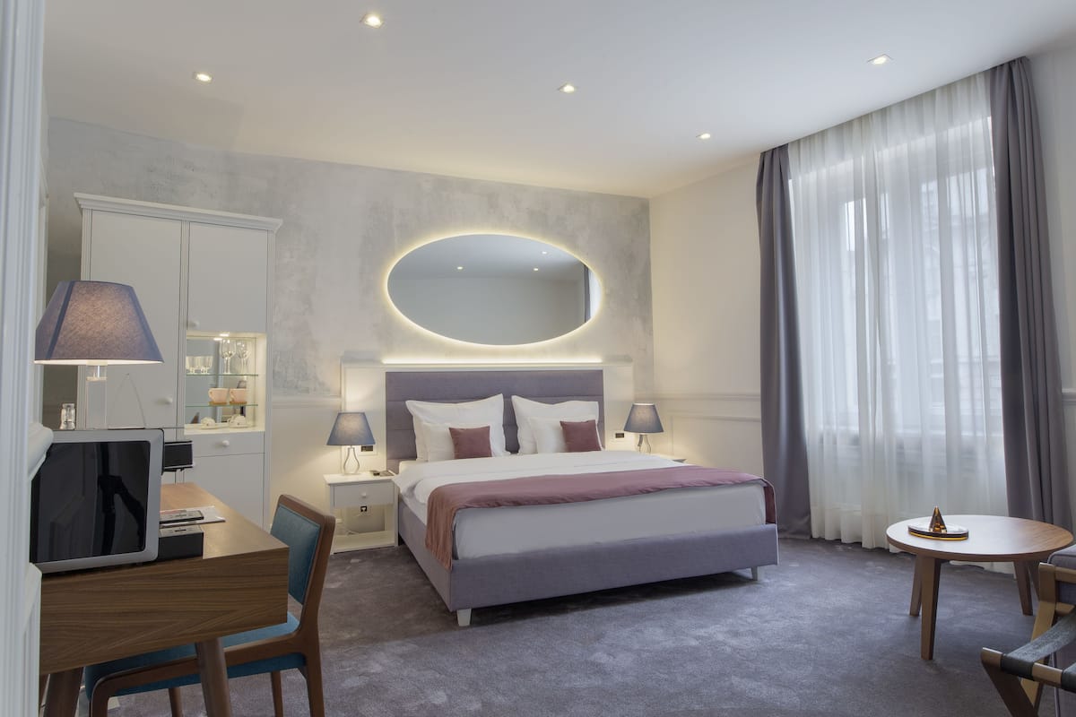 Una habitación de hotel moderna con una cama grande, mesitas de noche, un escritorio y una mesa redonda.