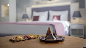A neatly arranged breakfast table with a plate of assorted nuts and dried fruits, a decorative glass container, and a bed with a modern headboard in the background. - Public House Hotel (Belgrade)