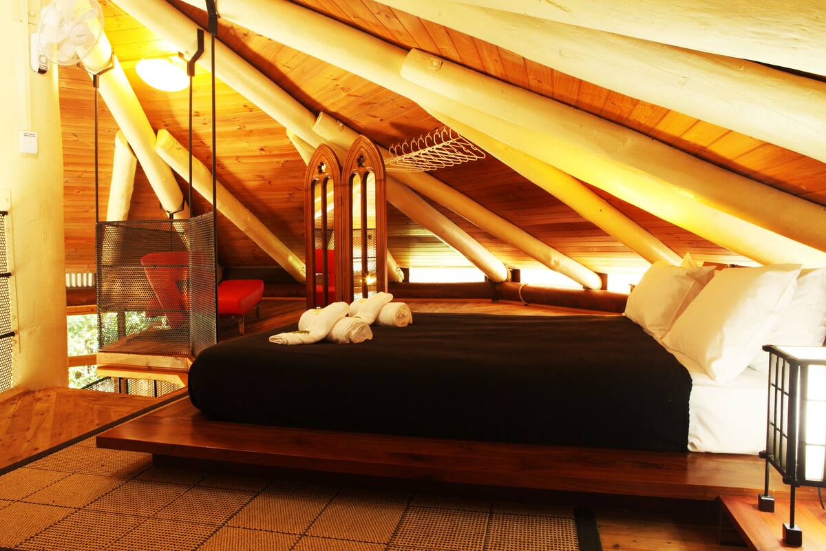 A room with a wooden ceiling, a bed with white linens, and a red chair.