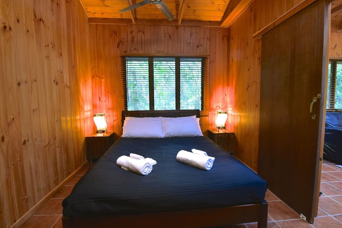 A wooden-paneled room with a bed, two bedside lamps, and a window with blinds.