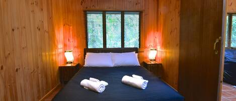 A wooden-paneled room with a bed, two bedside lamps, and a window with blinds.