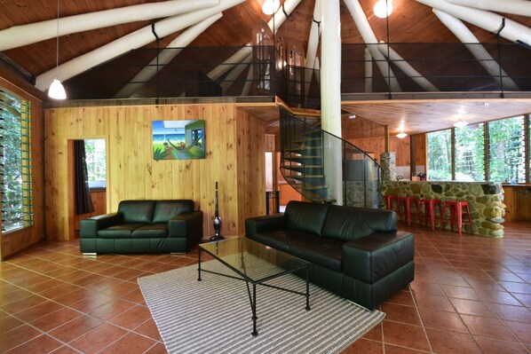 Un espacio habitable amplio con detalles de madera, una mesa de centro de vidrio y una escalera que sube a un nivel superior.
